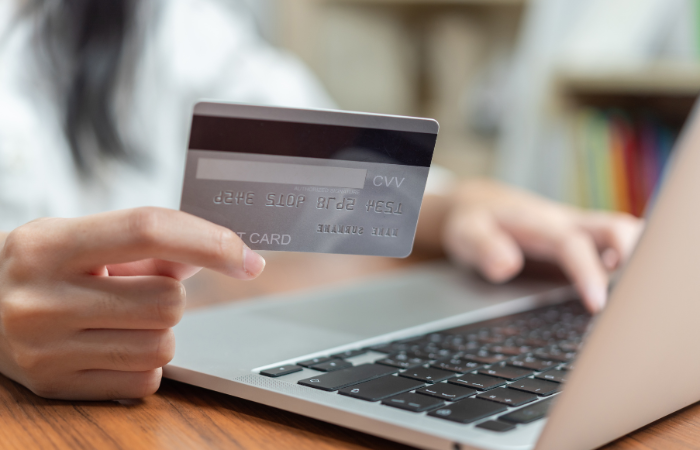  The image shows a person holding a credit card while typing on a laptop, likely engaging in an online transaction.