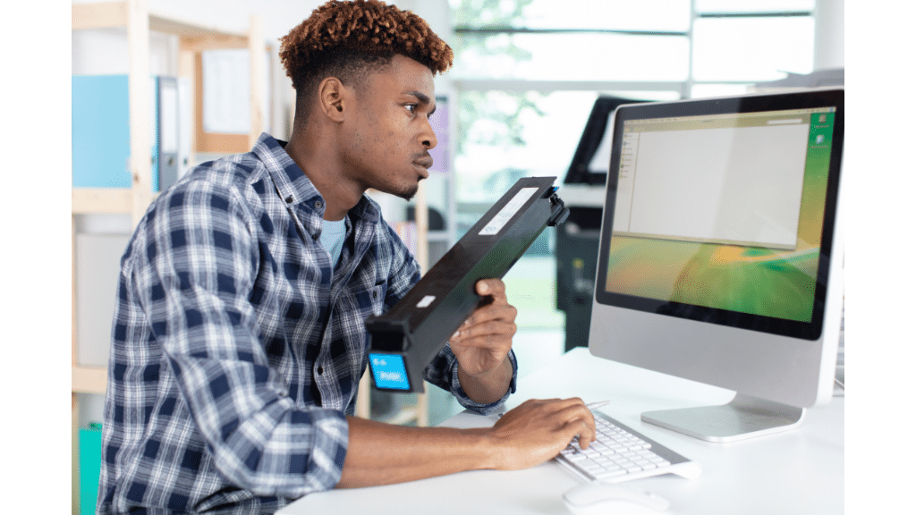 man holding a printer toner cartridge while using a computer