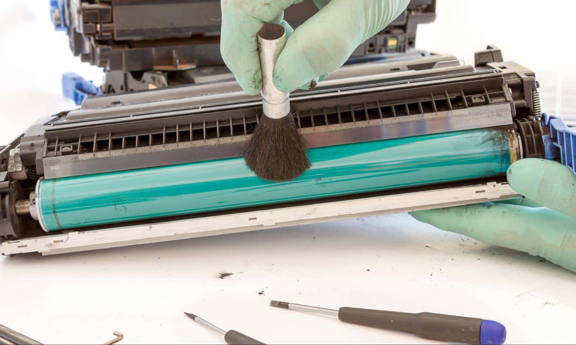 Person wearing protective gloves cleaning laser printer's toner drum with a small brush.